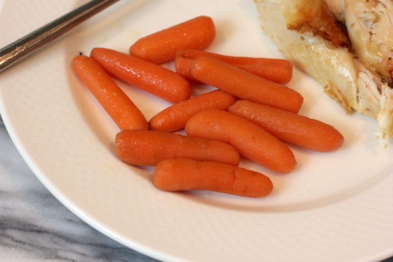A serving of tender slow cooker maple bourbon glazed baby carrots on a white plate.