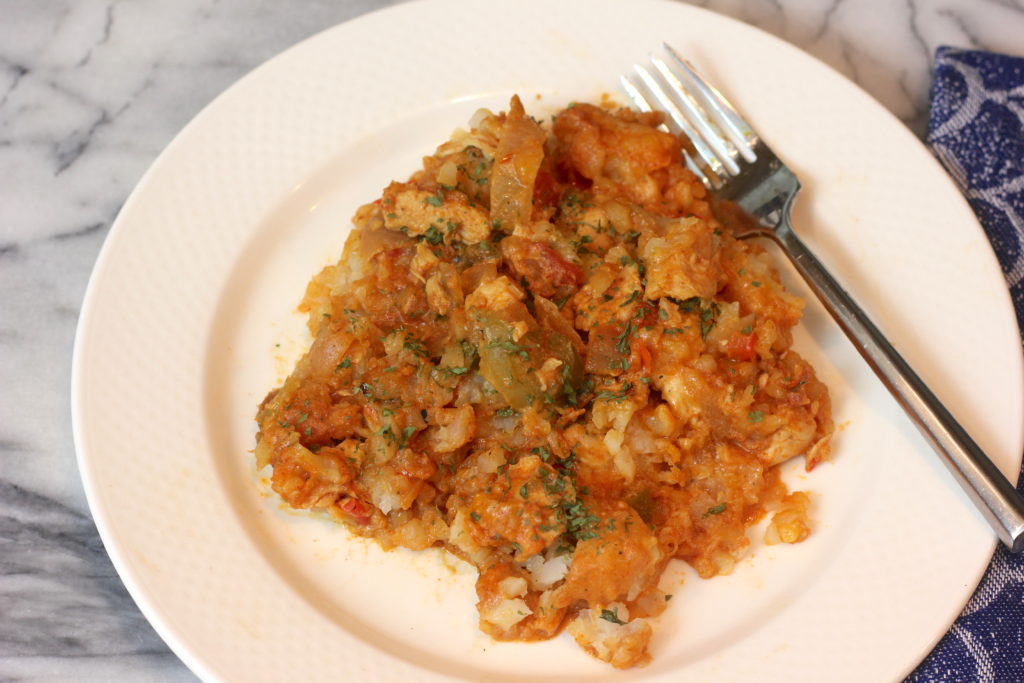 easy-mexican-chicken-tater-tot-bake-recipe-plated A top-down view of a serving of baked Mexican chicken and tater tot casserole garnished with green herbs, sitting on a white plate with a metal fork resting on the right side.